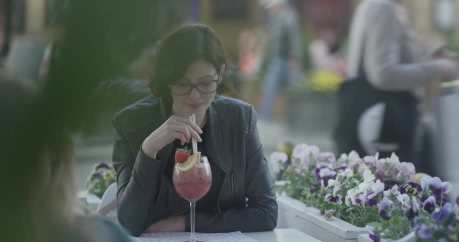 A woman stirs a cocktail with a straw before taking a sip through the straw