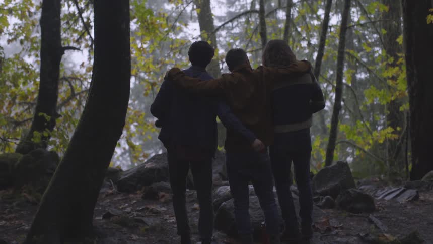 Man puts arms around friends while standing in forest