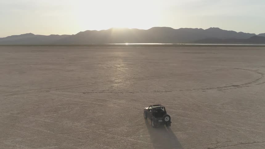 A jeep drives across a salt flat in the desert with mountains in the distance