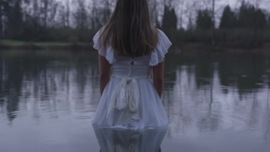 Woman in a white dress stands half submerged in a lake