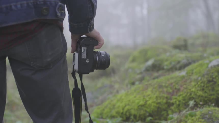 A man stands near a misty forest with a camera in his hand