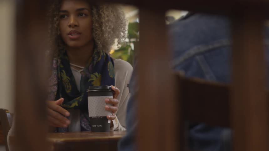 Young woman holding coffee talks to another person