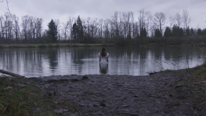 Woman wades into pond during winter under a hazy sky