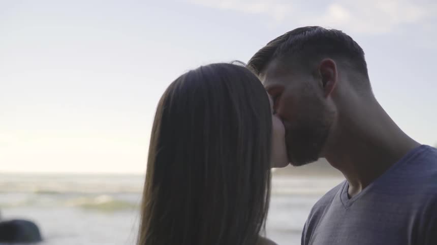 A man and woman kissing each other next to the sea