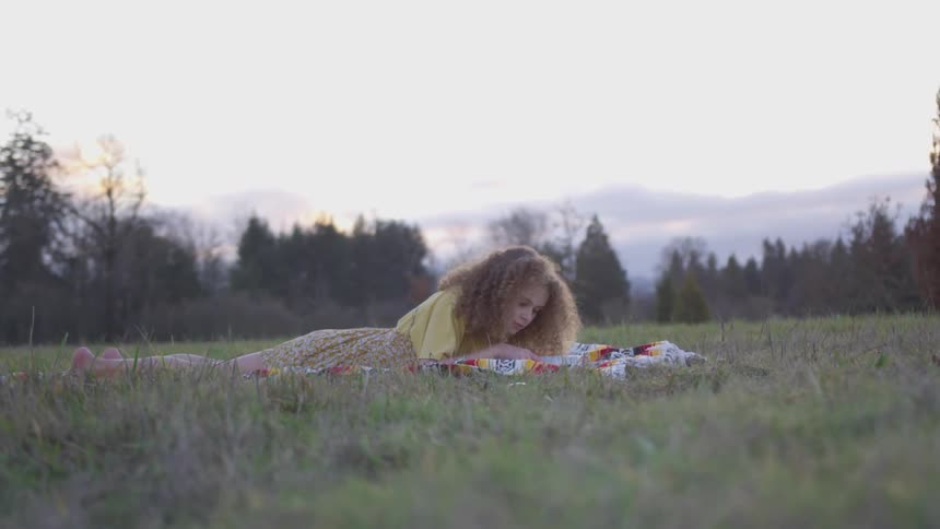A woman lays on her stomach on the grass and reads