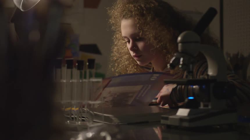 Young girl reads book at desk with test tubes and microscope