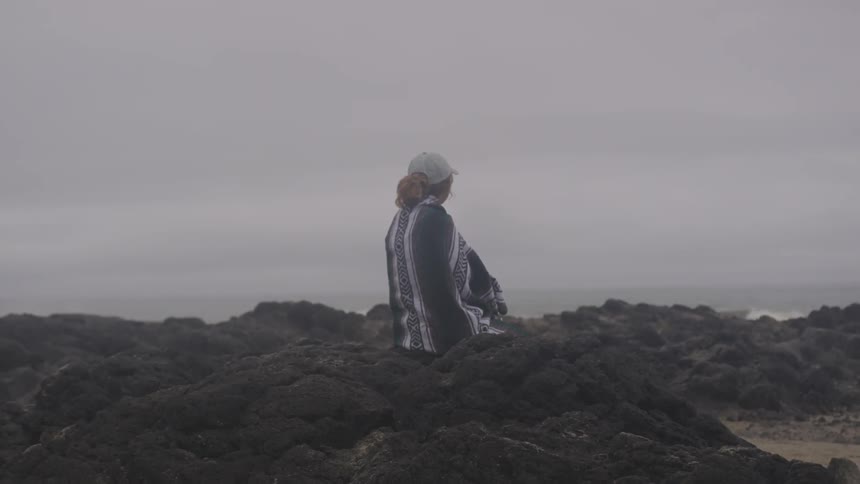 A woman sitting on some rocks next to the sea