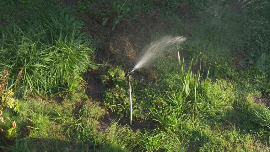 A sprinkler turns on and sprays water as it rotates