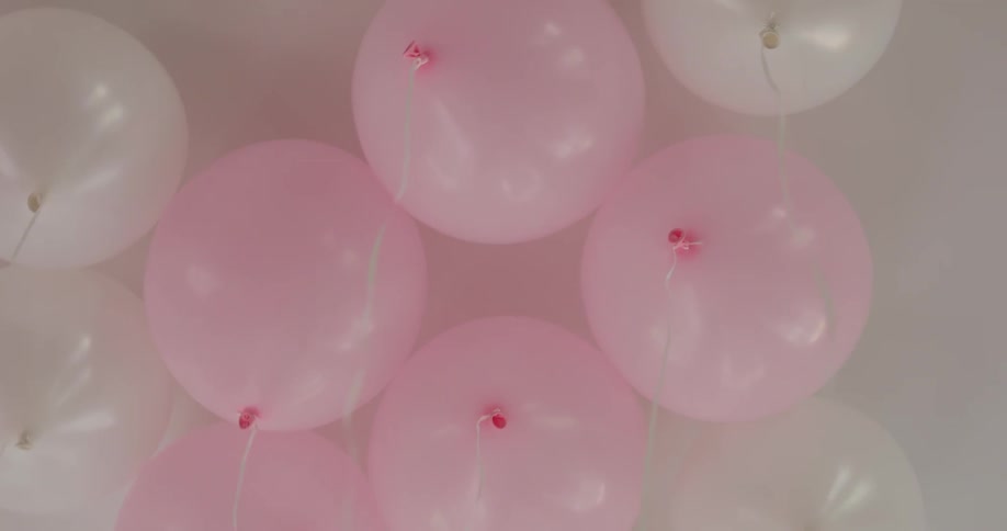 There are balloons on the ceiling that are pink and white