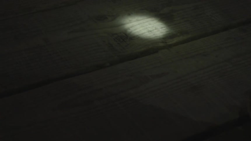 Person walks across floor boards using a flashlight