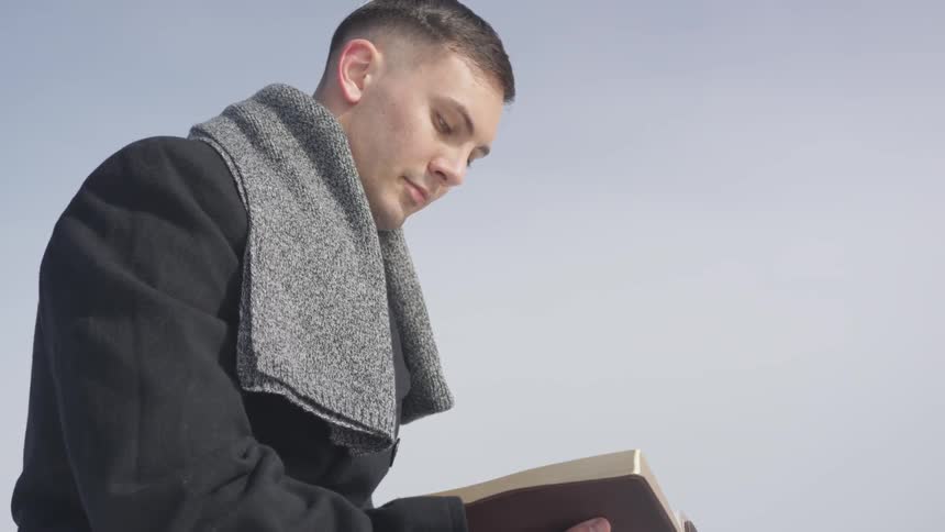 Male in a jacket looks down and reads the bible