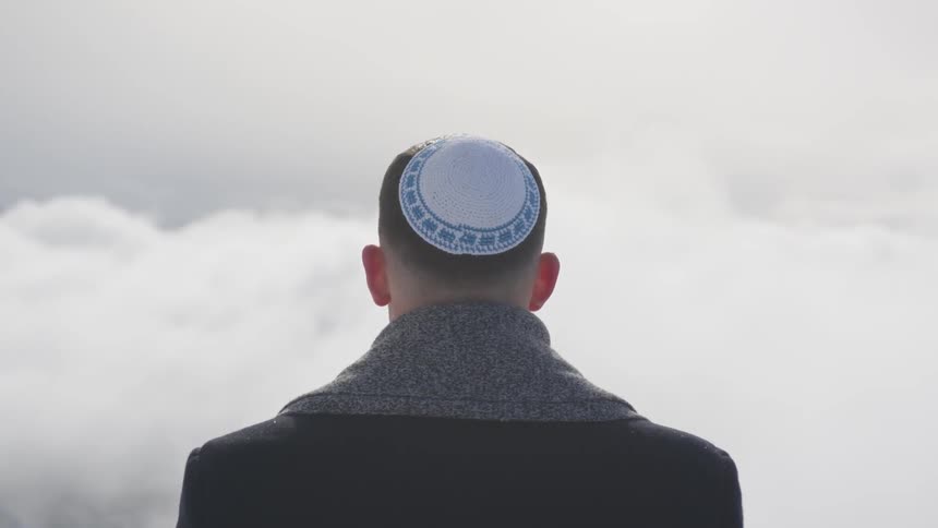 A man wearing a yamaka stares a puffy white clouds