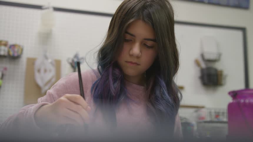 A girl paints on a white paper with a paint brush