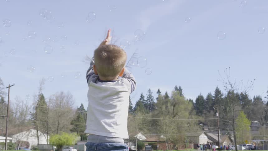 A young boy chases floating bubbles on a lawn