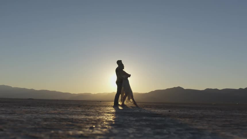A man and woman dance in the desert at sunset