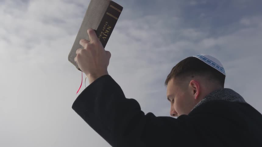 A man wearing a yamaka holds a bible over his head