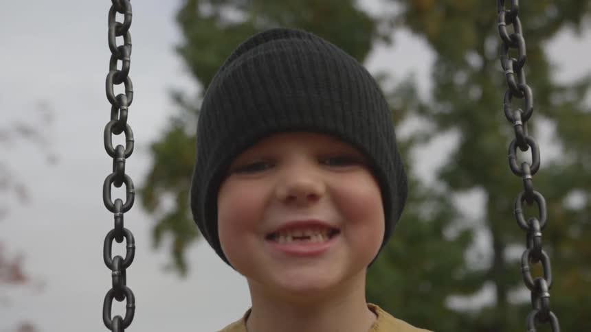 Boy sits on swing and smiles as teeth grow in