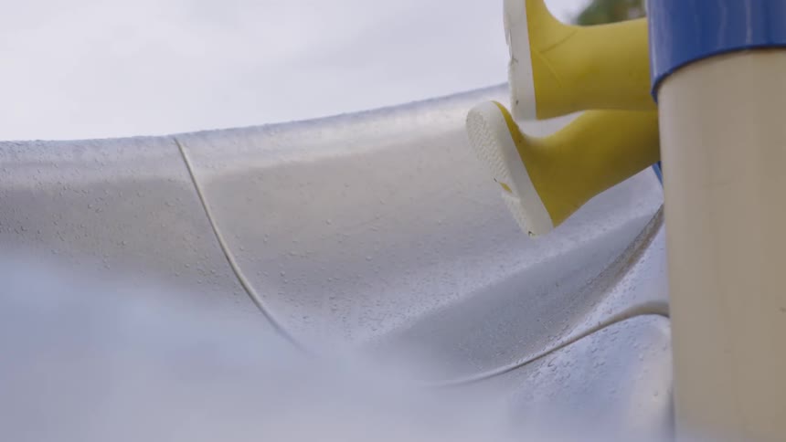 Little kid sitting at the top of a slide wearing yellow rain boots
