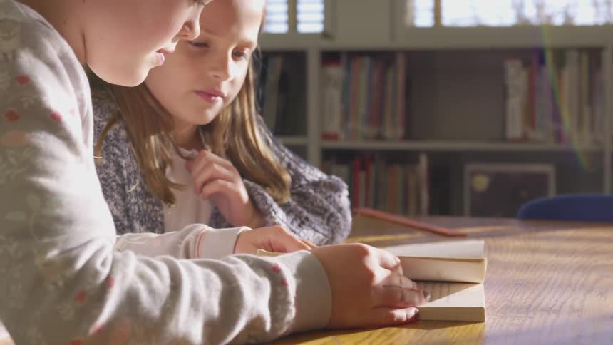 Two children sit and read a book together