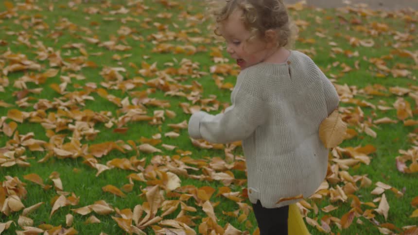 Small child in rain boots running through fall leaves