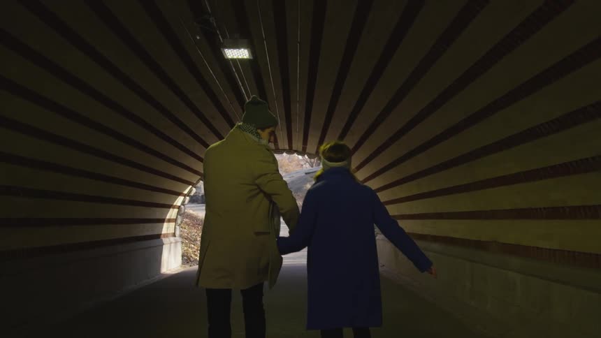 Woman and man walking holding hands on a tunnel