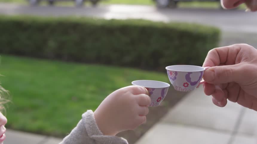 Little girl and father cheers with tiny tea cups outside on a rainy day
