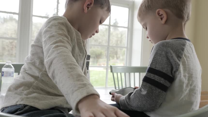 Two children sit on a table looking at a phone