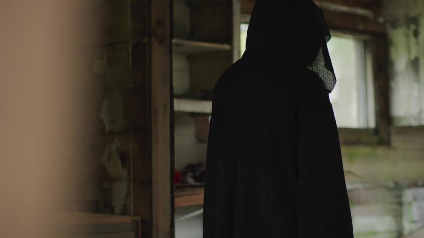 Hooded person looks at the wreck of a cabin
