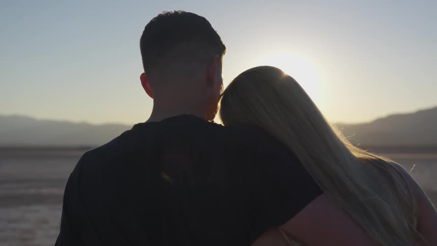 A man embraces and kisses a woman's forehead at sunset