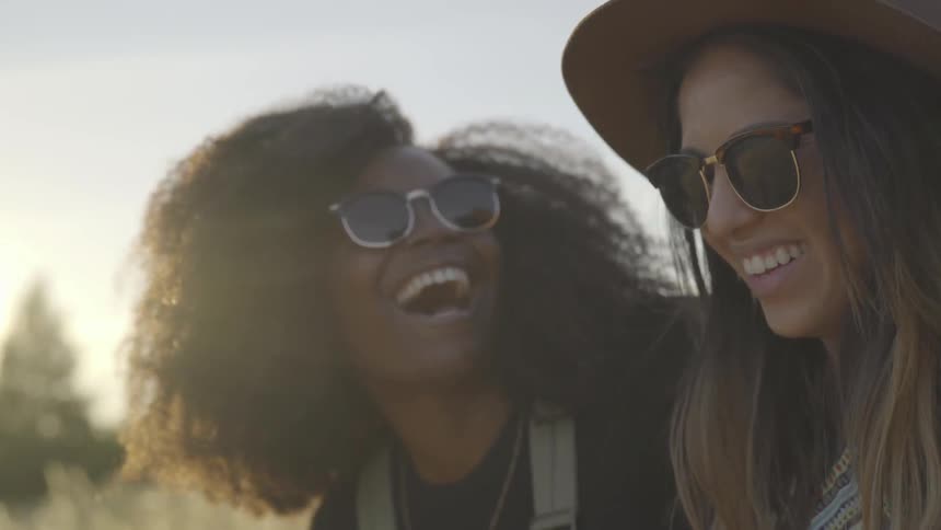 Two women laugh while sitting in a field at sunrise