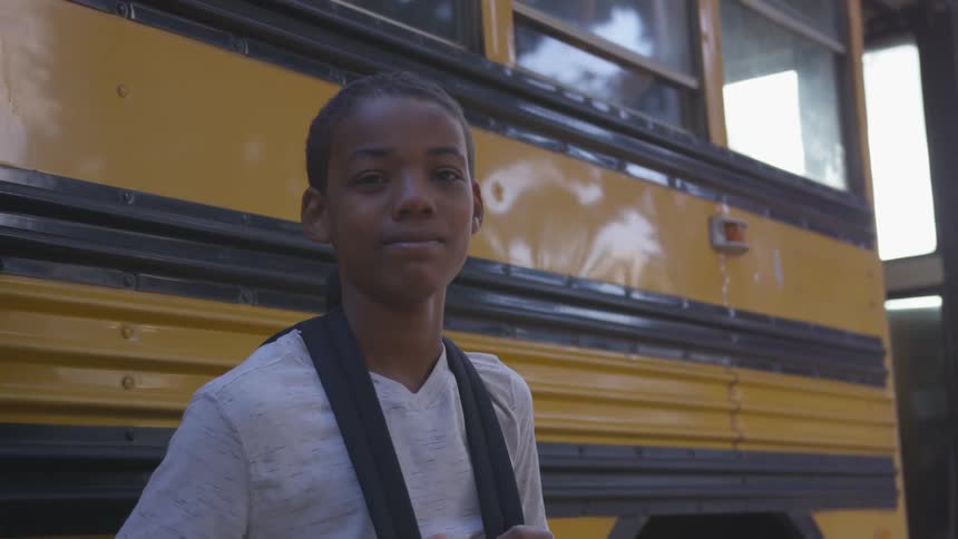 Young boy smiling next to a school bus