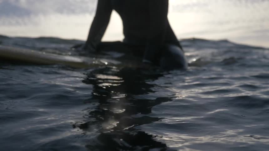 Woman in wetsuit sits on surfboard in ocean