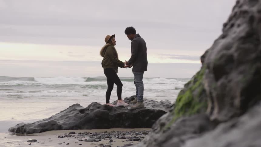 Man and woman holding hands on a boulder on a beach