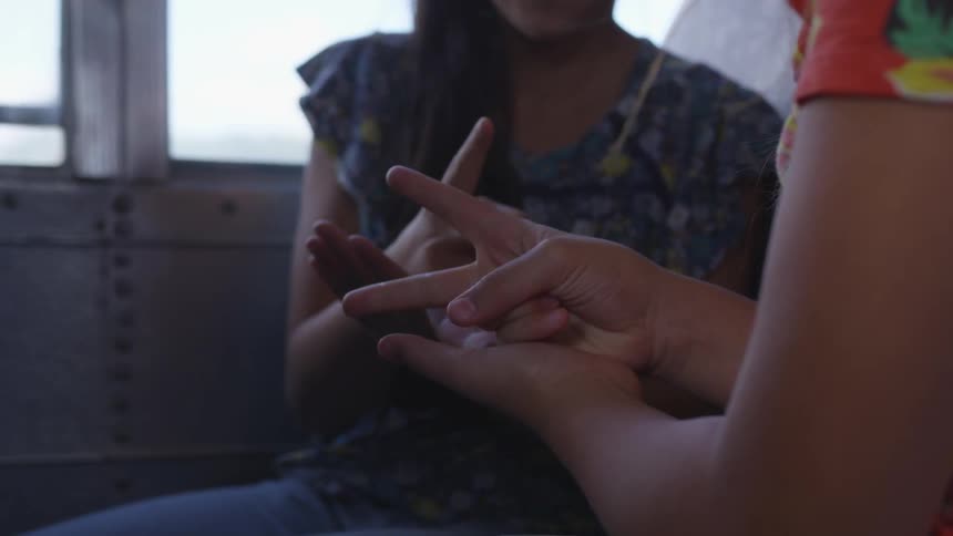 Girls sitting on a school bus play rock paper scissors