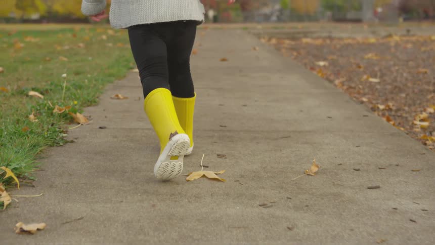 Girl in yellow boots runs along sidewalk