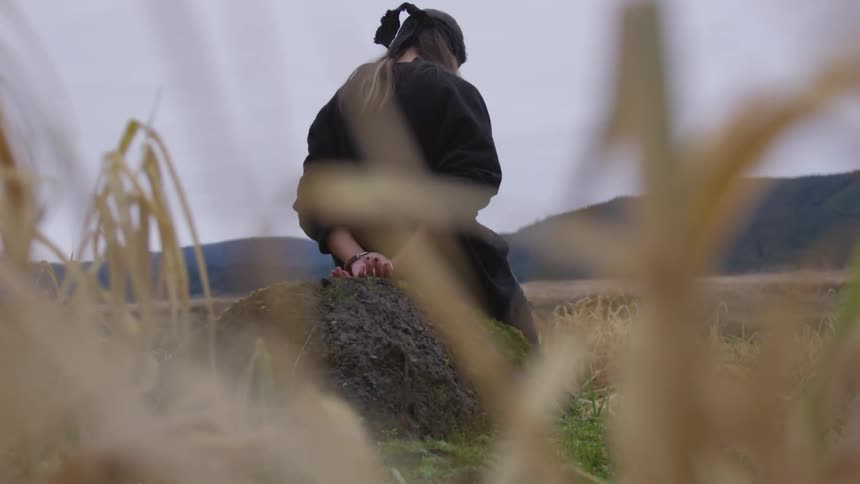 Person sits with hands behind their back in field near hills