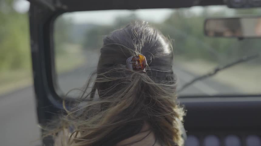 A woman drives a jeep down the road as the wind blows her hair