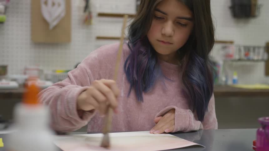 A young girl paints across a sheet of paper