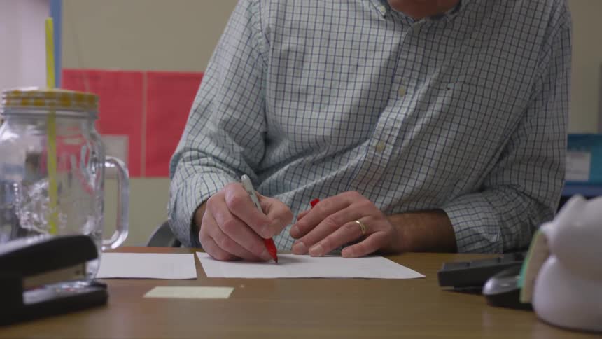 Man sits at table grading a paper in red ink