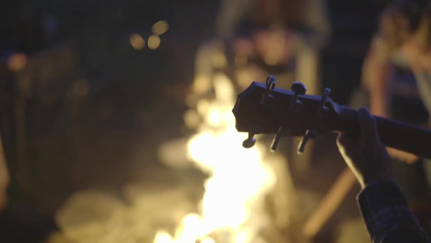 A group of people around a campfire one playing a guitar