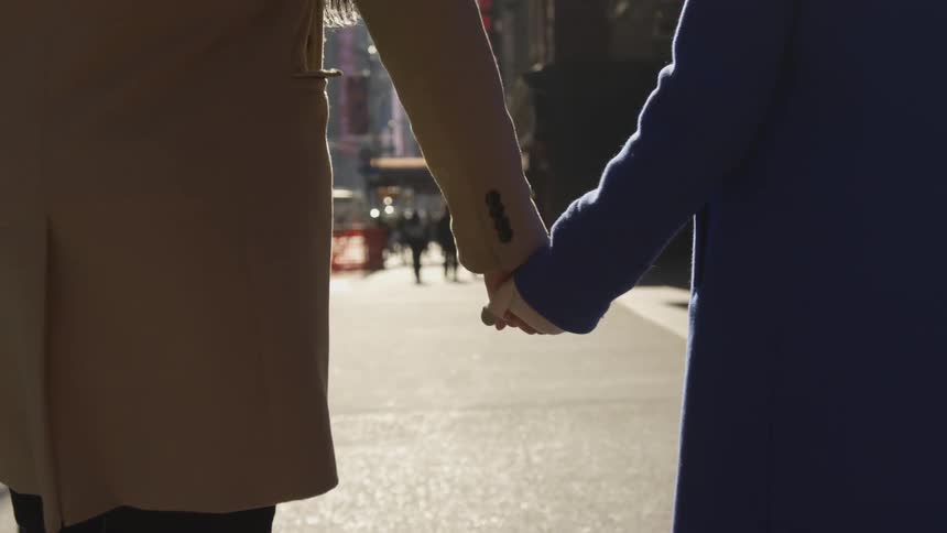Man and woman holding hands and walking through a city street