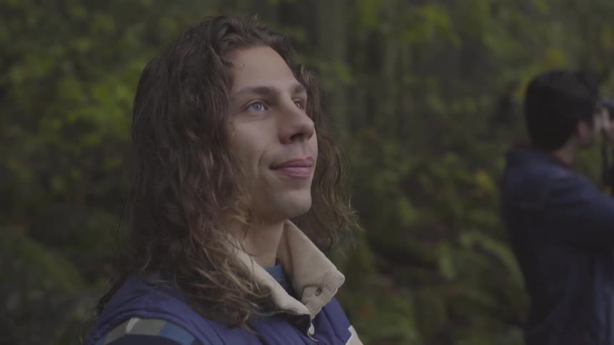 Man with long hair looks up and smiles in forest