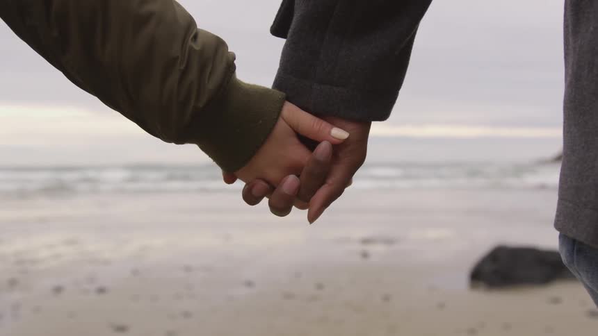 Two people hold hands on beach