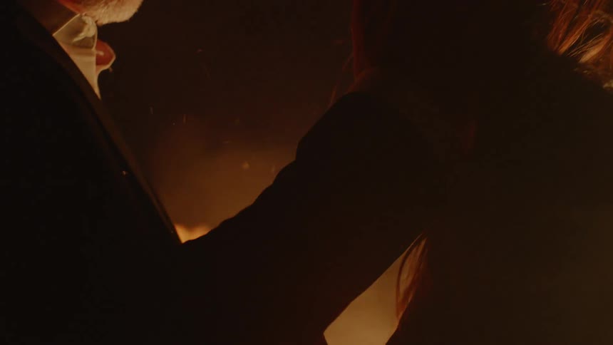 Man touches a woman's hair while fire burns beside them