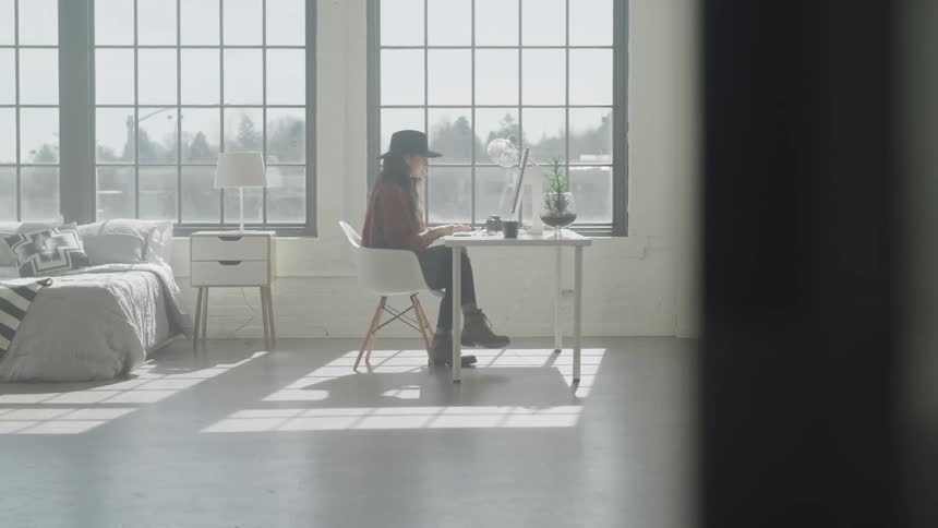 A person wearing a hat sitting at a desk and typing on a keyboard