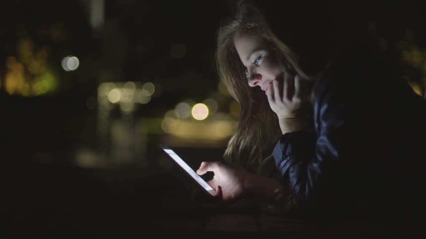 Woman laughs as she scrolls through her phone outdoors at night