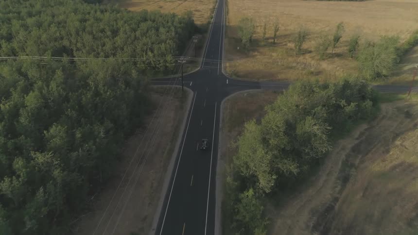 Car drives down a desolate road towards a crossroad surrounded by plains and trees