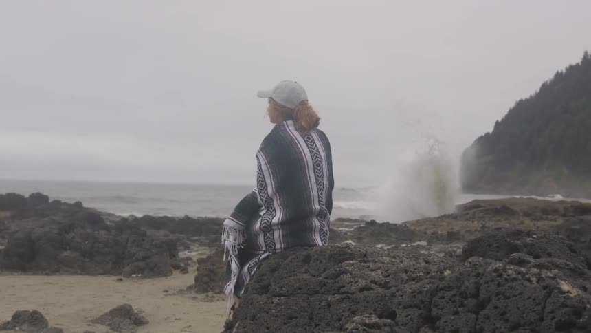 A woman sits on a rock by the ocean