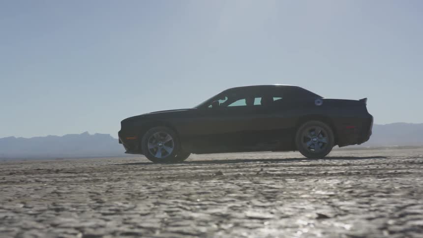 A black sports car driving in slow motion on the flat dirt surrounded by mountains