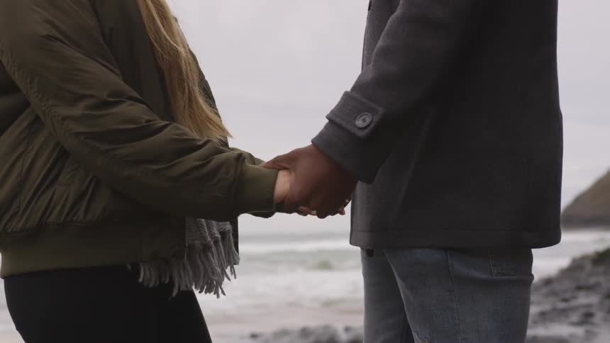 Two people hold hands by the beach